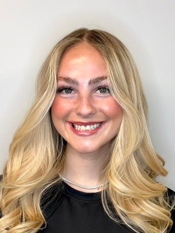Smiling blonde woman with curled hair wearing a black top against a light background