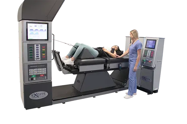 Person reclines on a medical treatment table beside a control console and monitor in a clinical room
