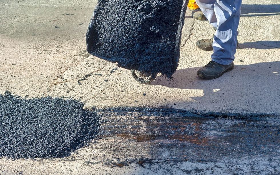 A person is spreading asphalt on a concrete surface.