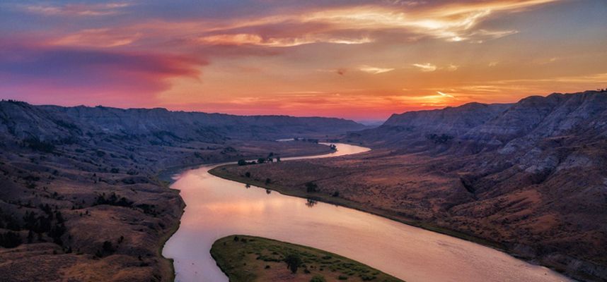 An aerial view of a river surrounded by mountains at sunset.