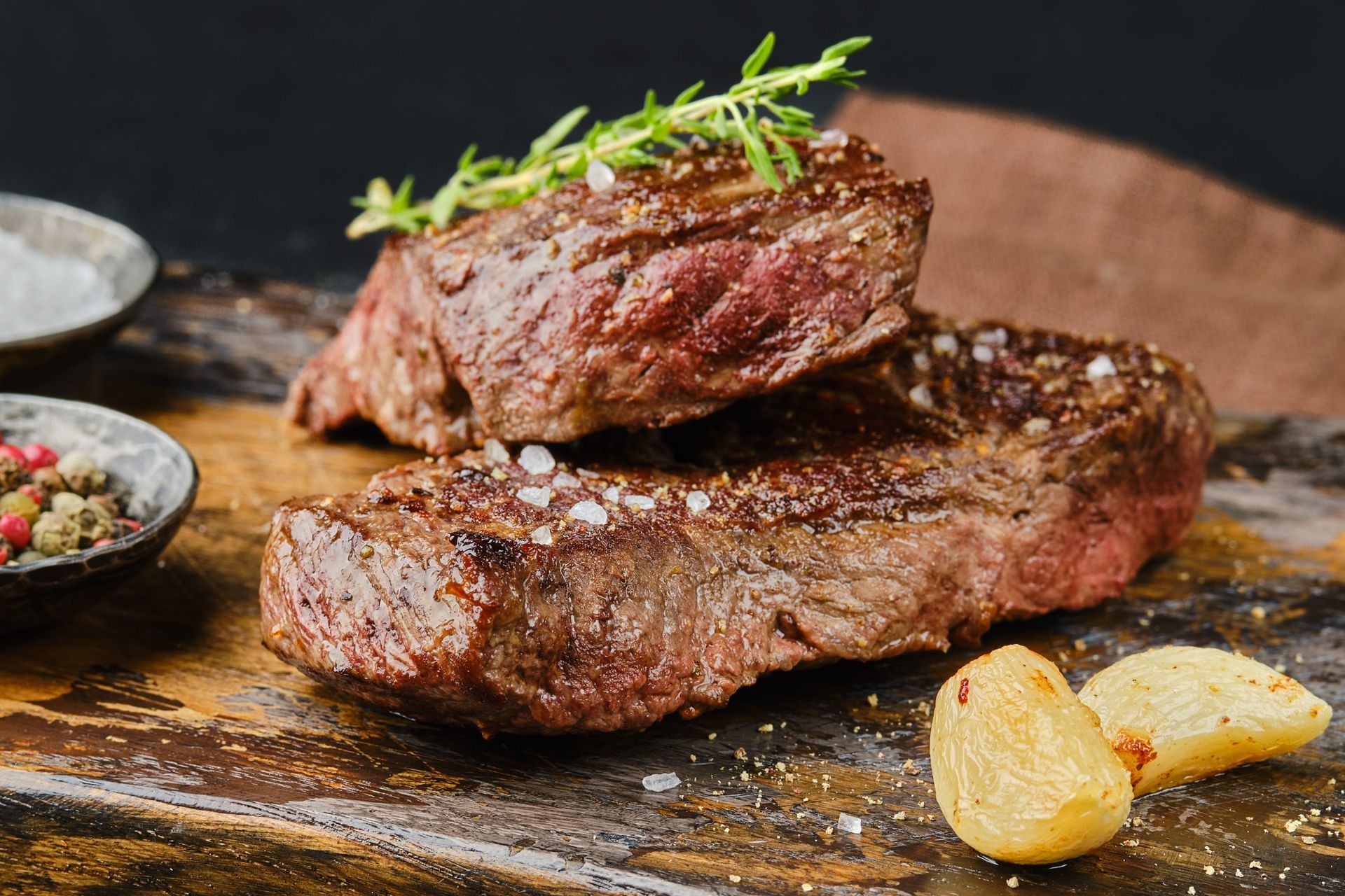 Two steaks are stacked on top of each other on a wooden cutting board.