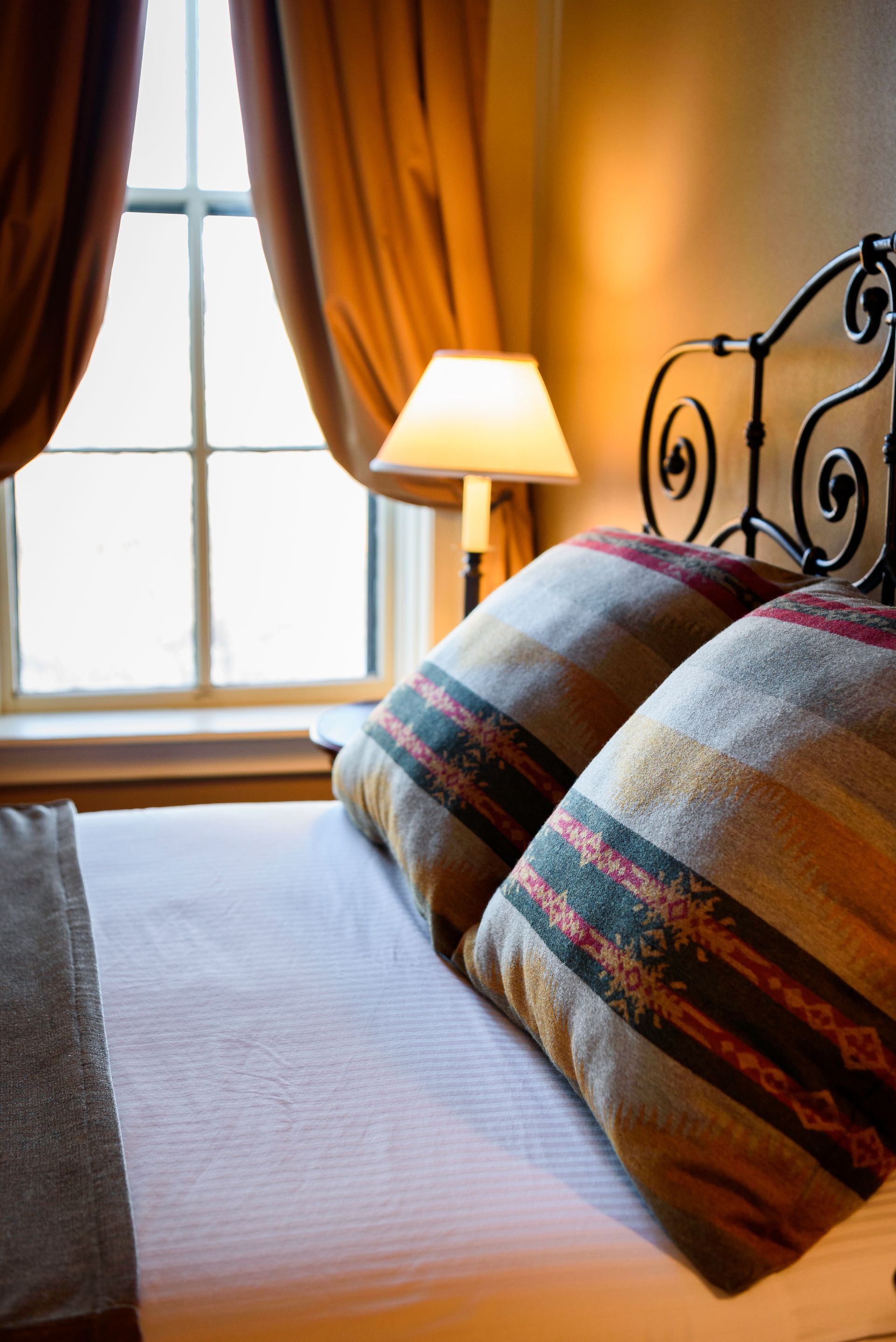 A bed with two pillows and a lamp in front of a window