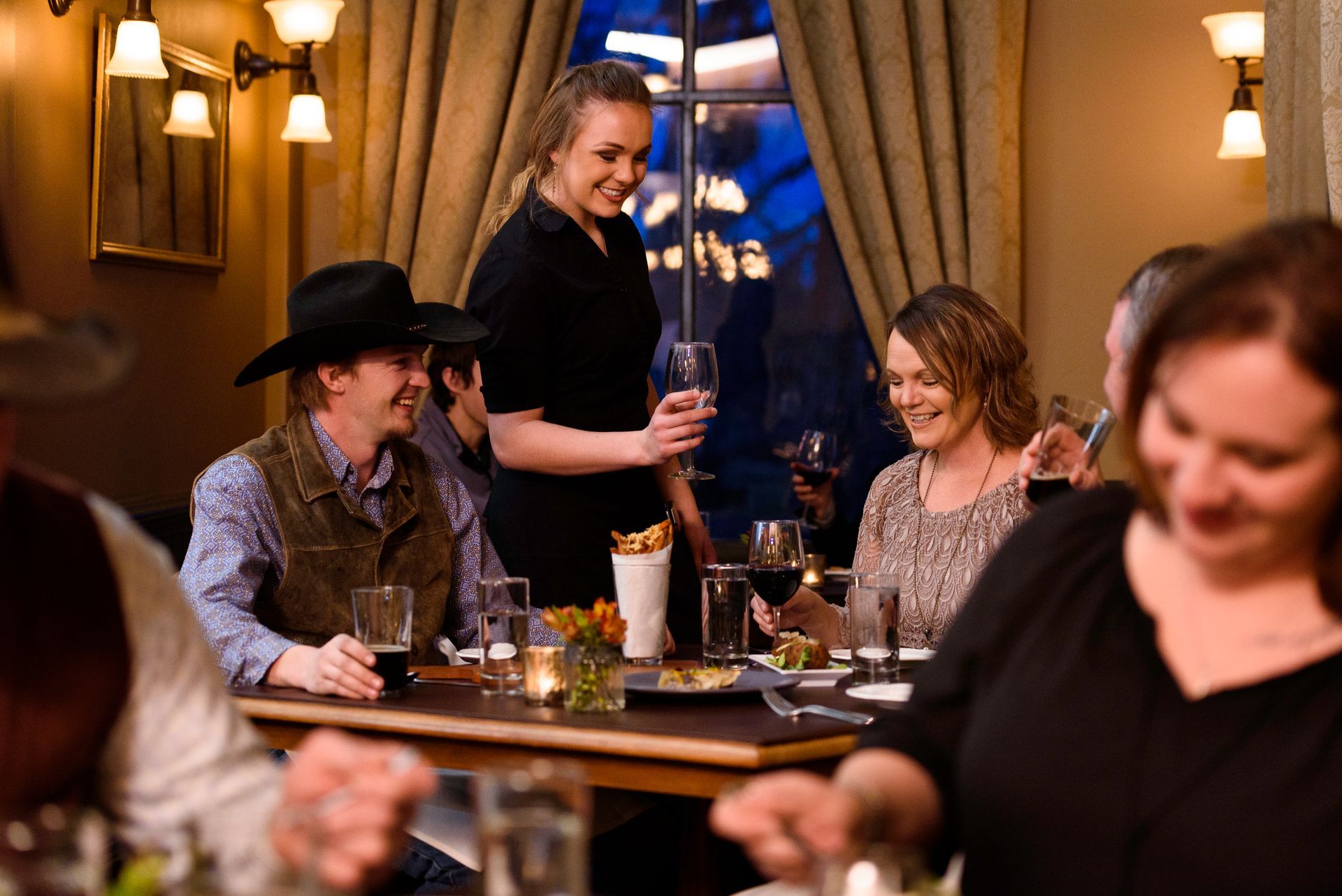 A woman is serving a glass of wine to a group of people sitting at a table in a restaurant.
