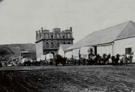 A black and white photo of a horse drawn carriage in front of a large building.
