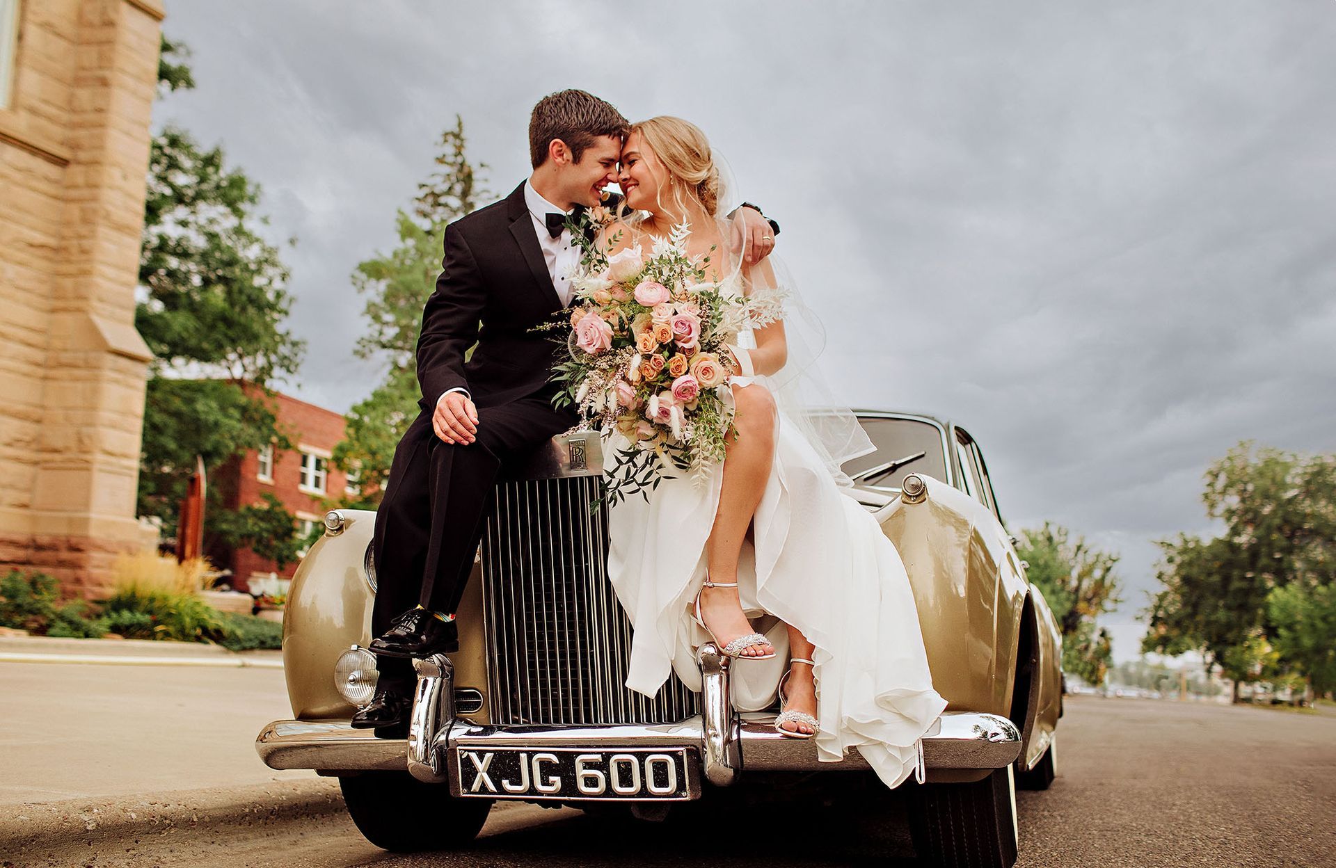 A bride and groom are kissing on the back of a vintage car.