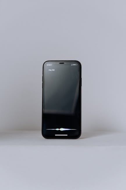 Smartphone standing upright on a plain gray surface with a dark screen and Siri-style voice indicator.