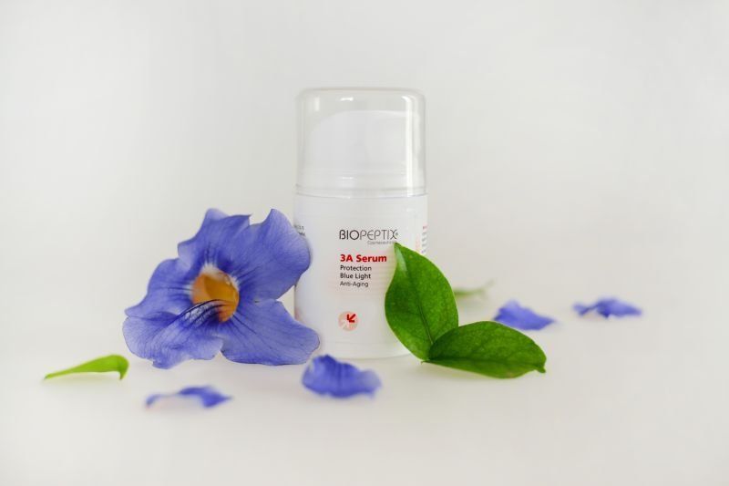 White cosmetic bottle with purple flowers and green leaves on a white background