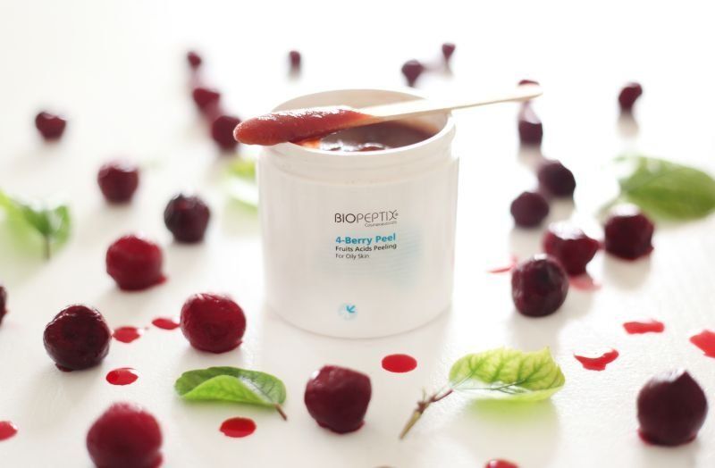 White cosmetic cream jar with berries and leaves scattered around on a white background
