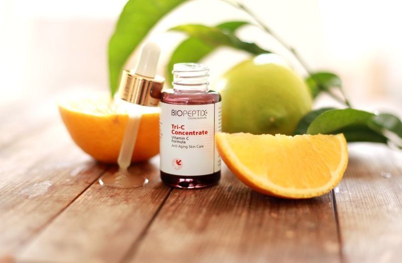 Bottle of citrus essential oil with orange slices on a wooden table, with green leaves in the background