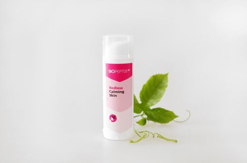 Pink cosmetic bottle with white cap beside green leaves on a light background