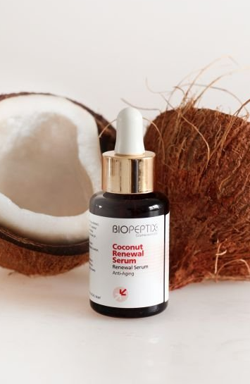Coconut serum bottle with dropper beside a halved coconut on a white background