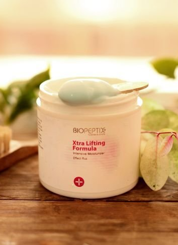Beauty cream jar with mint-green applicator on a wooden surface, with cucumber slices beside it