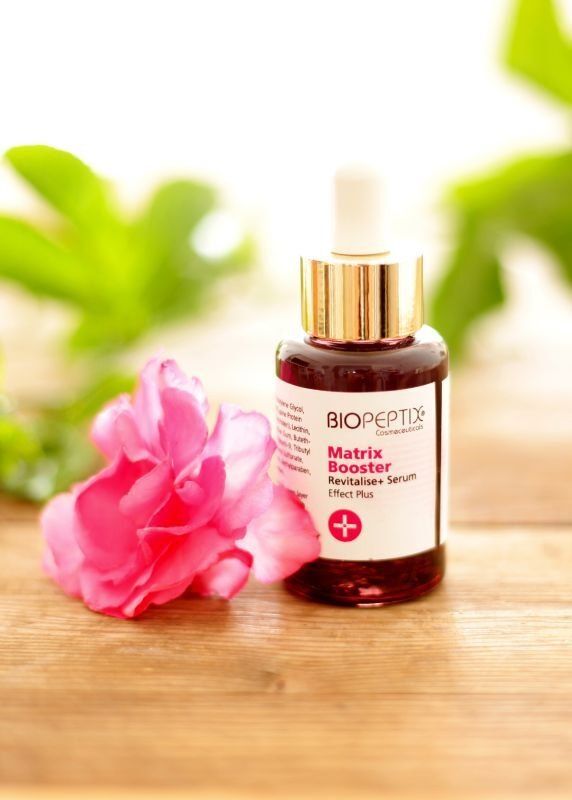 BioEffect serum bottle with dropper beside a pink flower on a wooden surface
