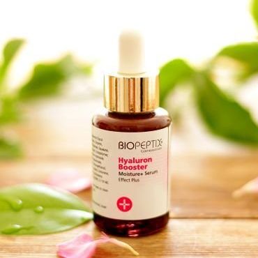 BioPeptix Hyaluron Booster serum bottle with dropper on a wooden surface, surrounded by green leaves