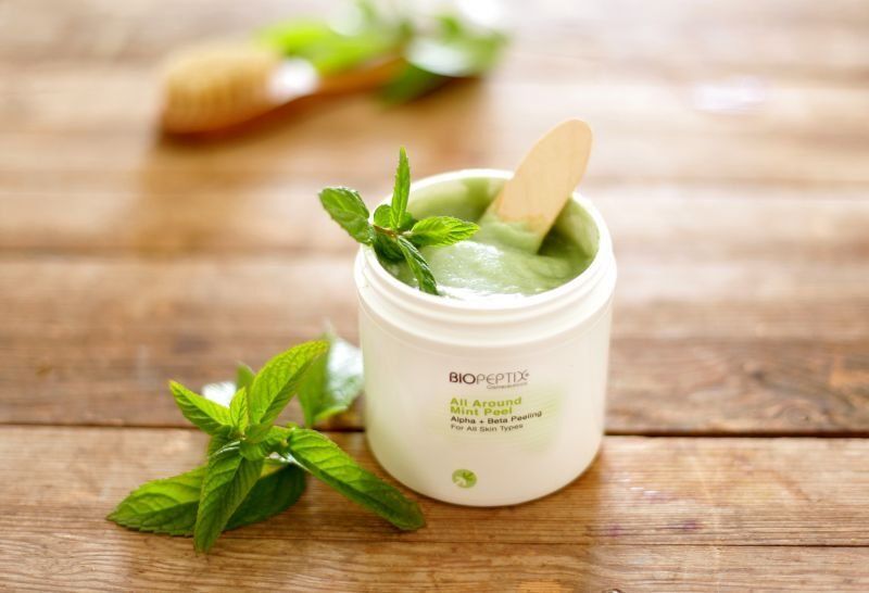 Herbal skincare cream in a white jar with mint leaves on a wooden table