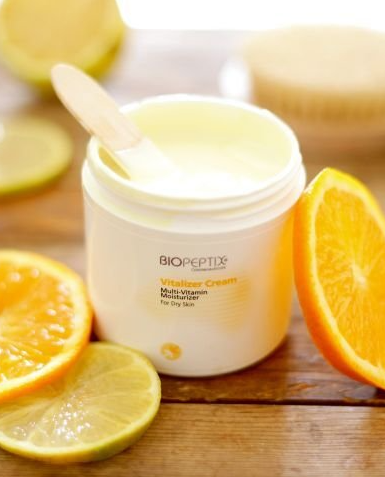 White cream jar with spoon, surrounded by orange and lime slices on a wooden surface
