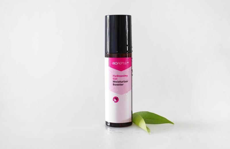 Pink cosmetic bottle with black cap beside a green leaf on a white background