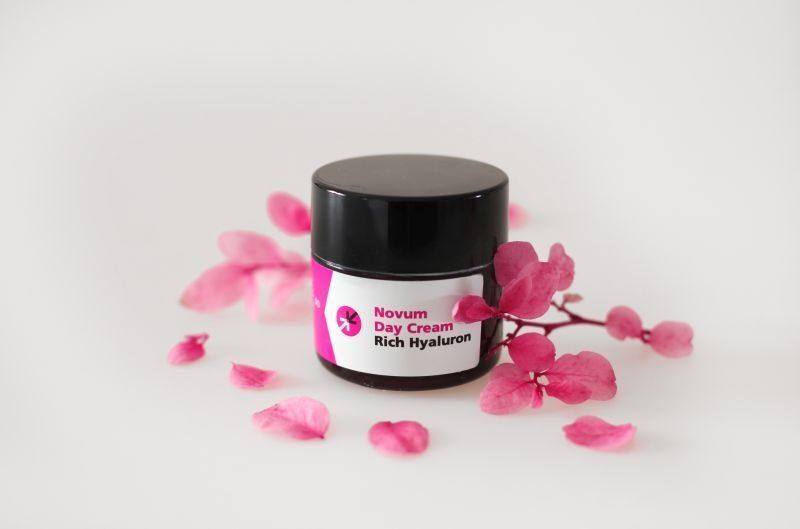 Black jar of pink body cream with petals scattered around it