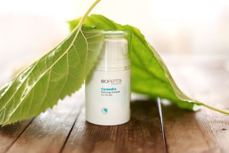White cosmetic bottle under a green leaf on a wooden surface, lit softly in the background
