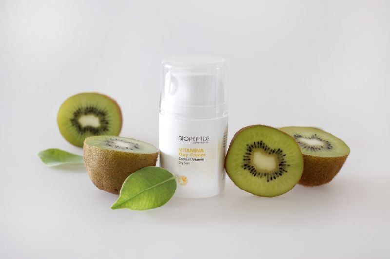 Kiwi skincare bottle surrounded by sliced kiwifruit on a white background