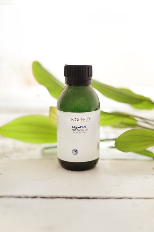 Small green glass bottle with black cap and white label, set against a white background with green leaves.
