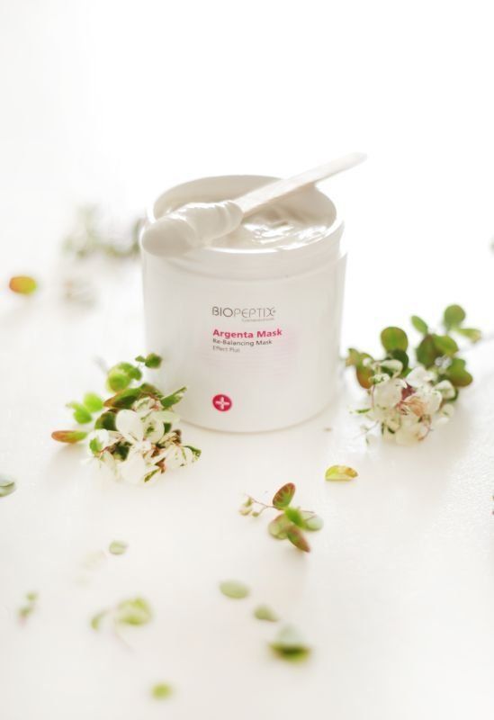 White skincare cream jar with a spatula, surrounded by small white flowers on a bright surface