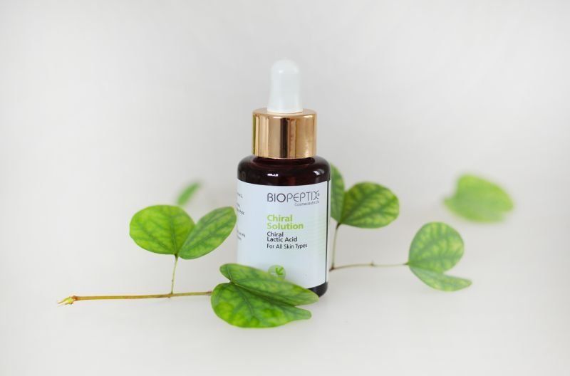 Skincare serum bottle with dropper and green leaves on a white background