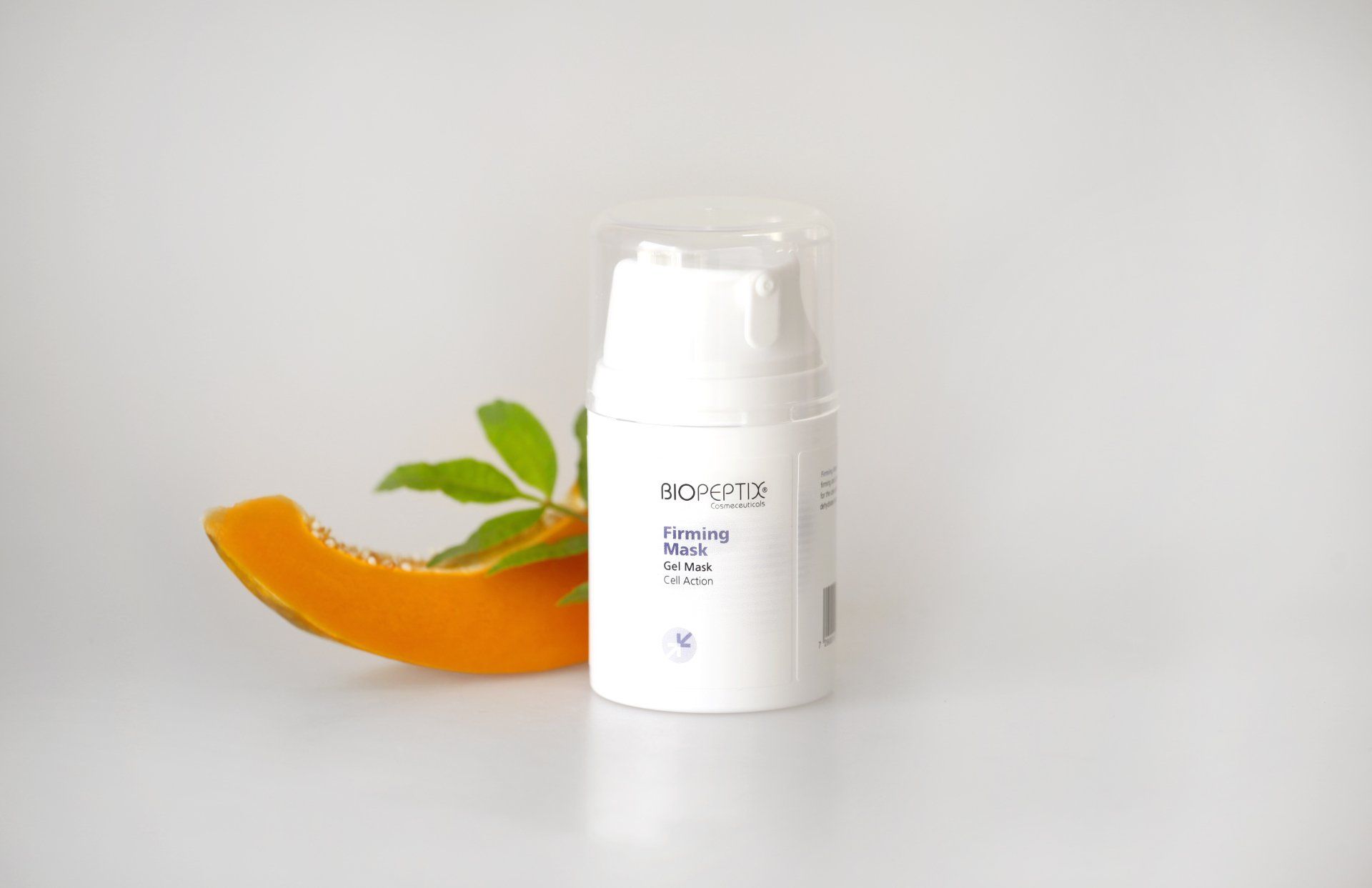 White cosmetic bottle with a clear cap beside an orange slice and green leaves on a light background