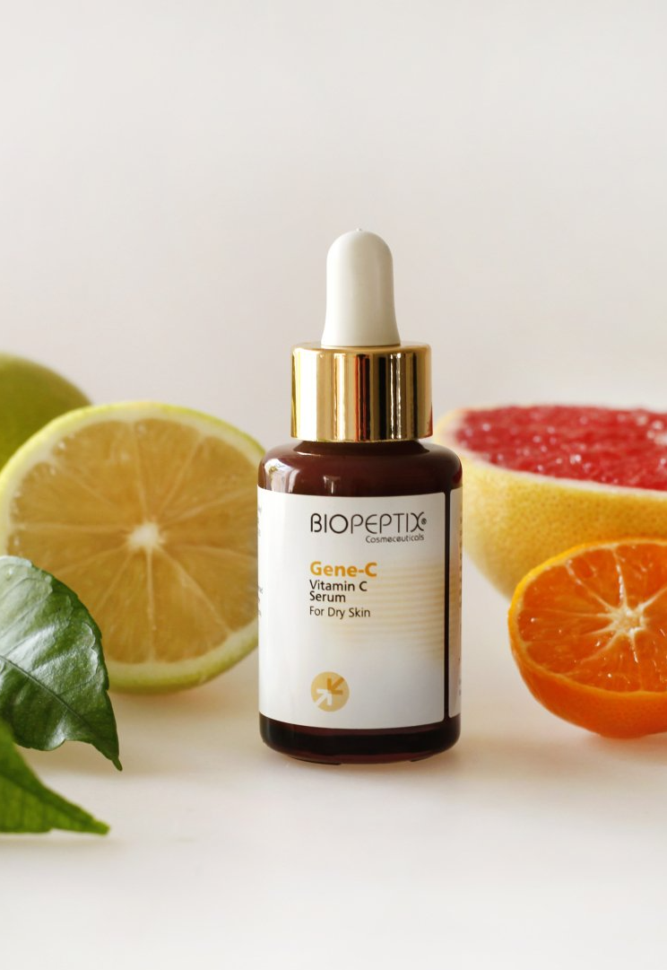 Bottle of citrus facial serum with dropper, surrounded by lemons, lime, grapefruit, and orange slices