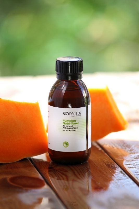 Brown essential oil bottle on a wooden table, framed by orange slices with a blurred green background