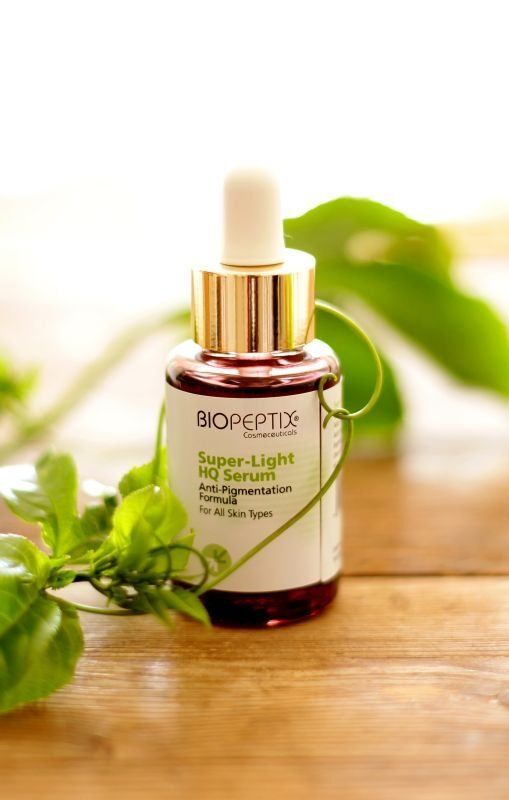 Drops of green botanical serum in a glass dropper bottle on a wooden table with leaves in soft light