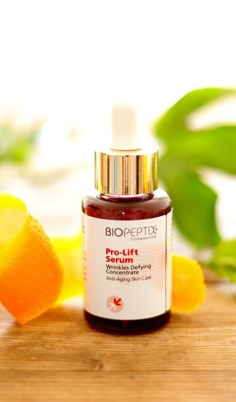 BIOPEPTE serum bottle on a wooden surface with oranges and green leaves in the background