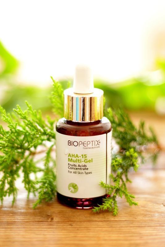 BIOPEPTIDE skincare serum bottle with gold cap on a wooden surface, framed by green foliage and soft light