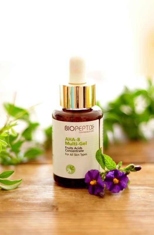BIOPEPTID serum bottle on a wooden table with green leaves and purple flowers on a bright white background