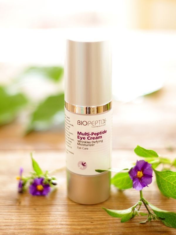 Biotique skincare bottle with gold cap, surrounded by purple flowers on a bright white background