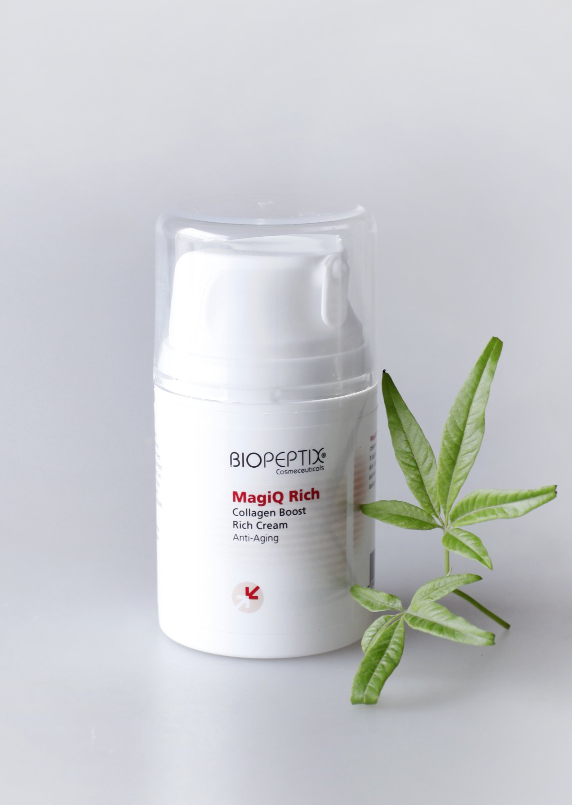 White skincare bottle with clear cap and green leaves on a light gray background