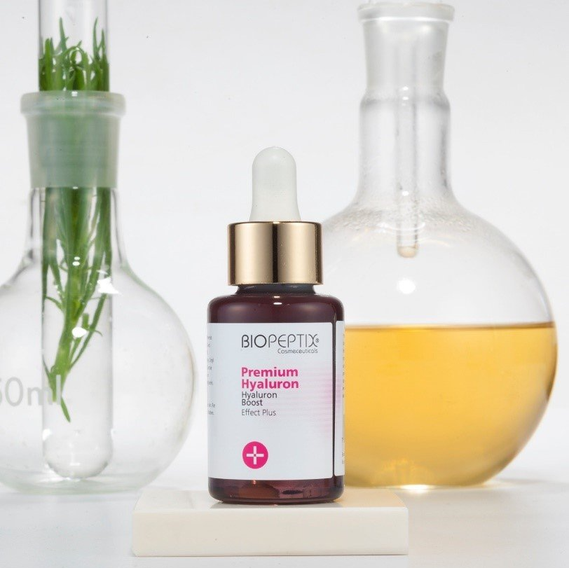 Skincare serum bottle with dropper between two glass lab flasks of liquid and herbs