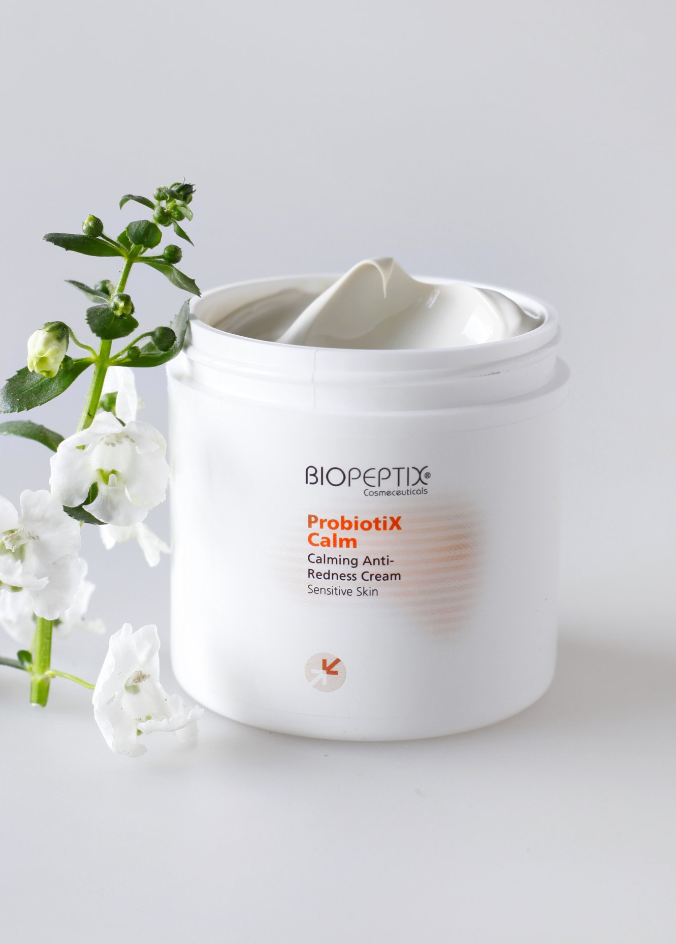 White skincare jar with lid removed, featuring a green vine and white flowers on a light background