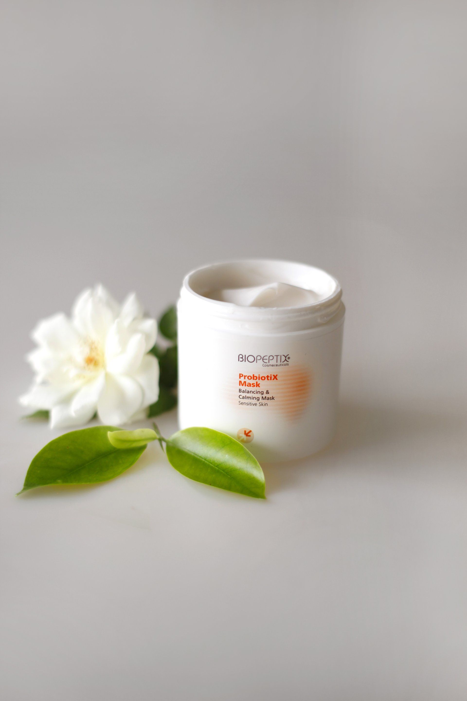 White cosmetic jar with a flower and two green leaves on a gray background