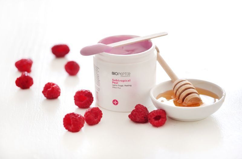Skincare jar, scoop, honey dipper, and red berries on a white background