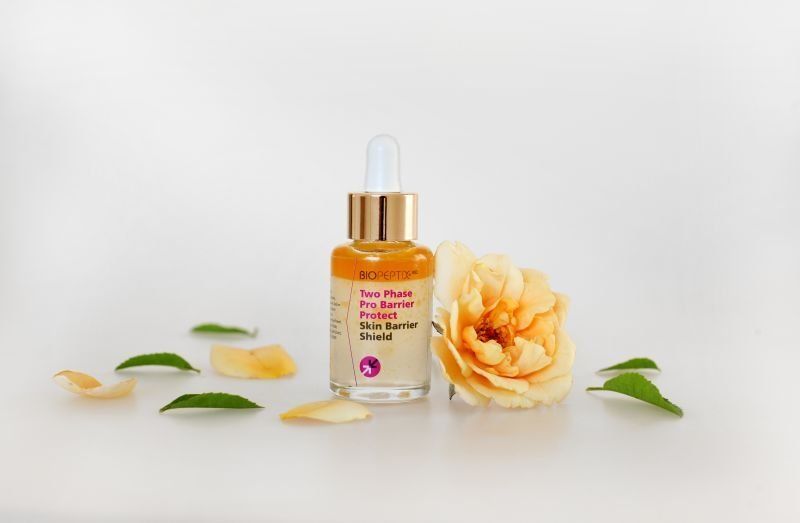 Dropper bottle of orange serum with peach rose and green leaves on a white background