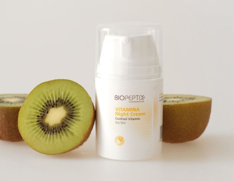 White Biopetix vitamin C cream jar centered with halved kiwis on a light background