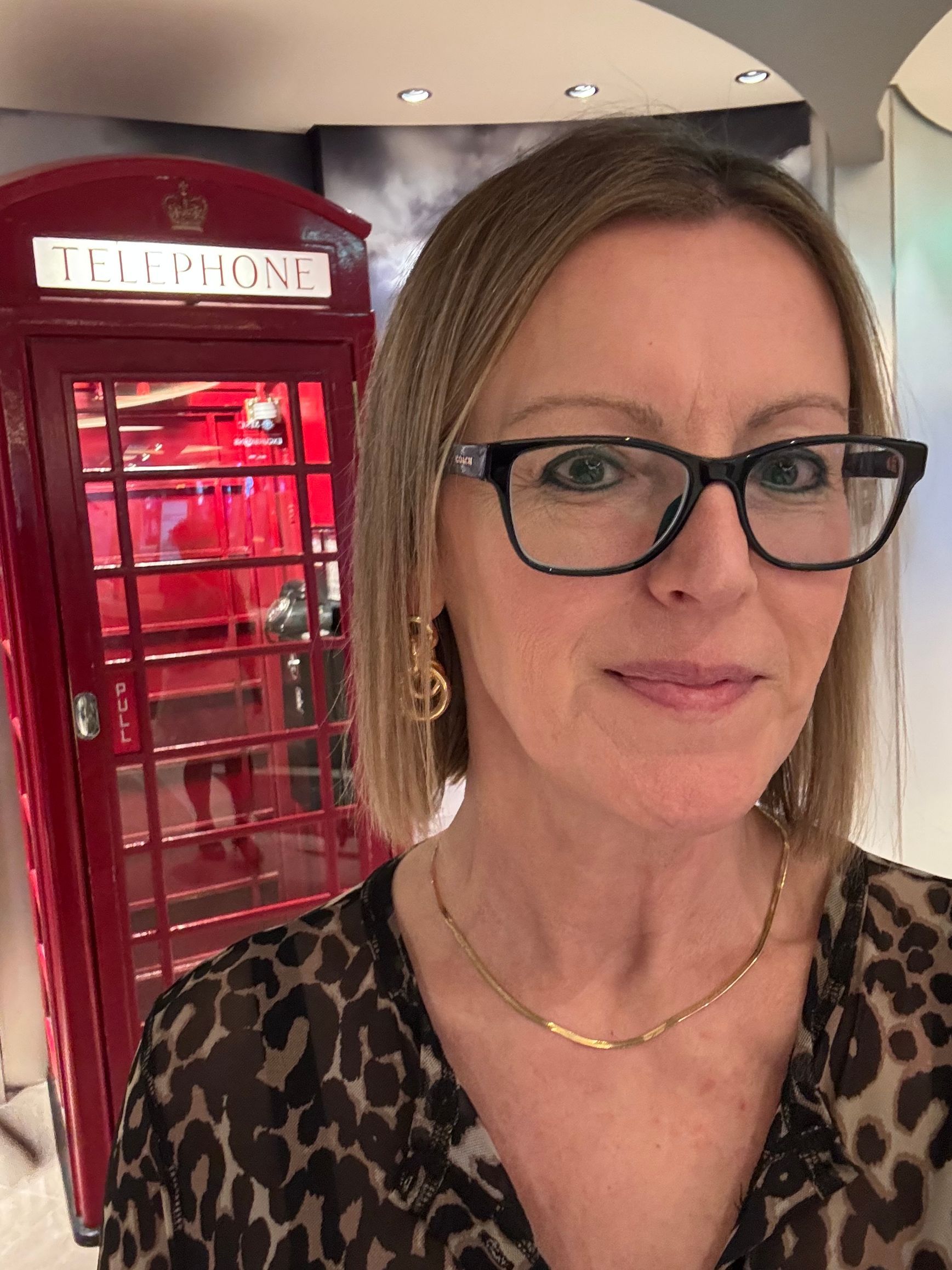 Woman wearing glasses in front of a red British-style phone booth indoors