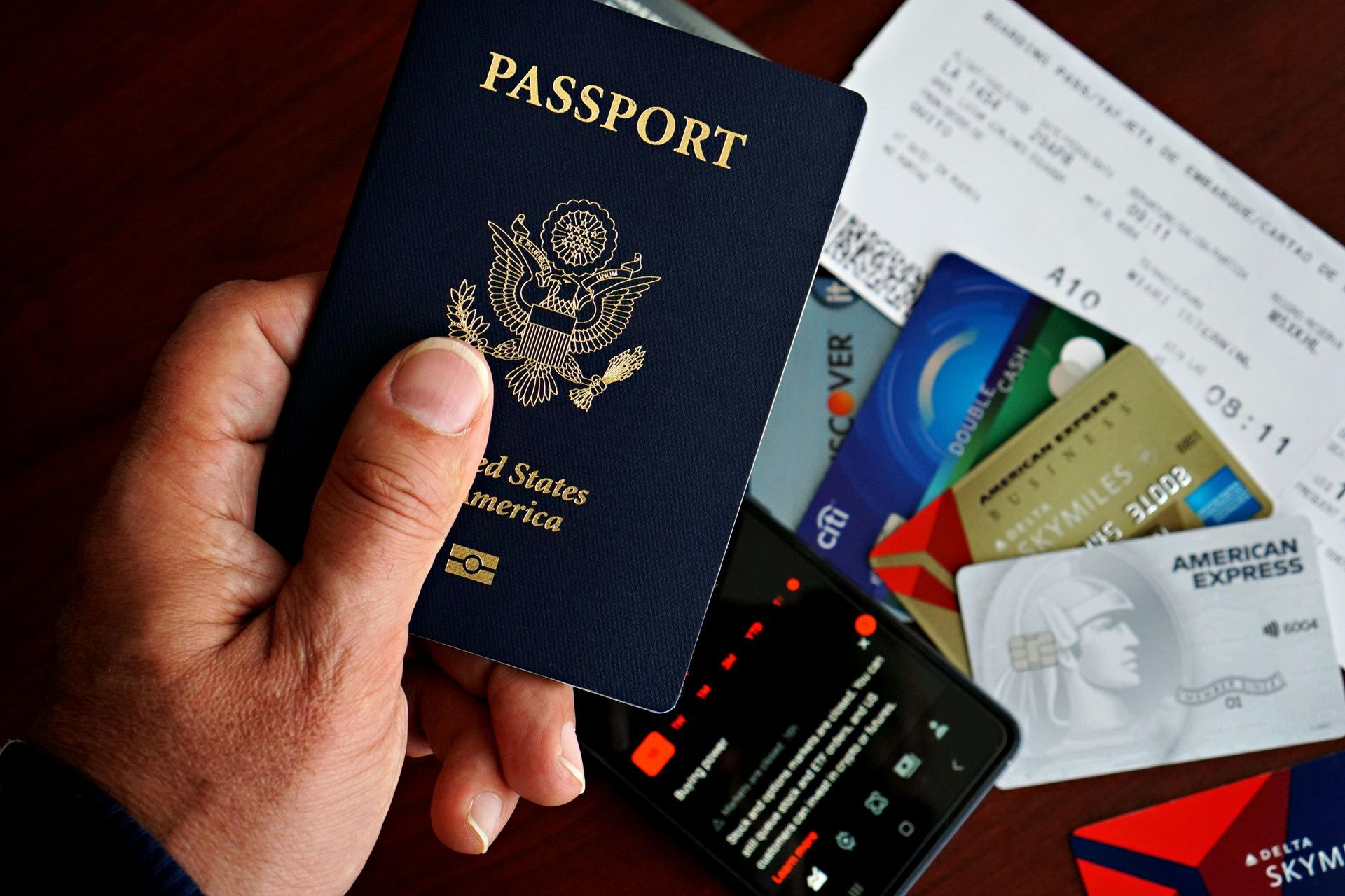 Hand holding a passport in front of several credit cards on a desk.