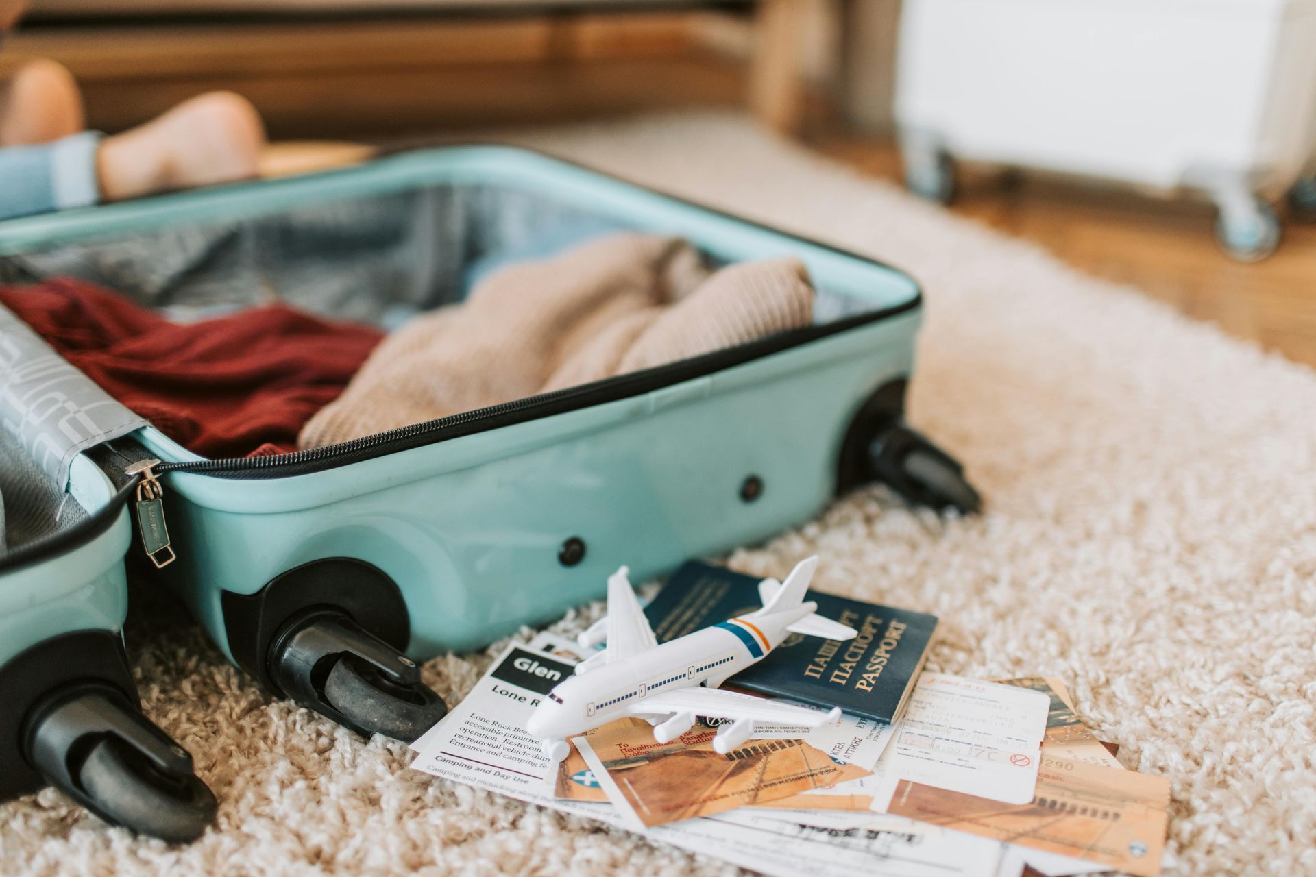 Open suitcase with clothes and travel papers scattered on a carpeted floor