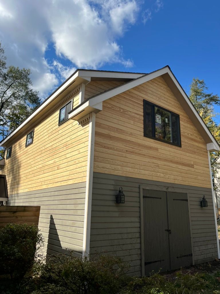 Two-story building with green siding on the bottom and light brown wood shingles on the top. Black doors and windows.
