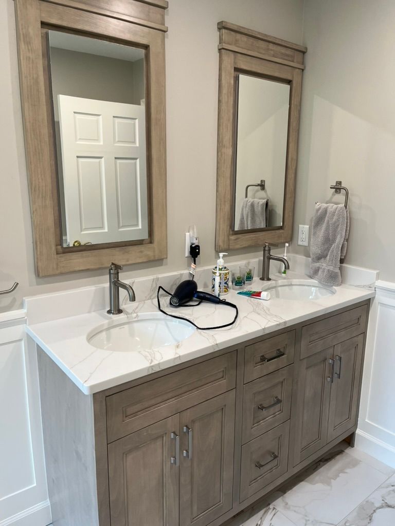 Double sink bathroom vanity with light wood cabinets, quartz countertop, and framed mirrors.
