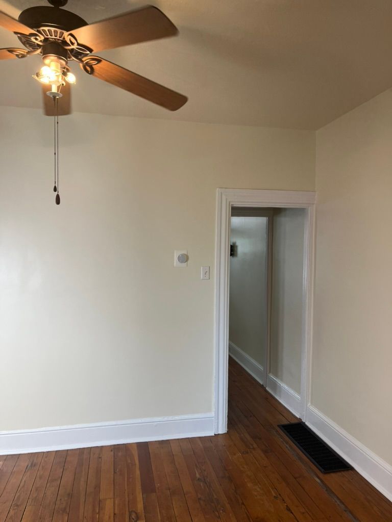 Empty room with wood floors, light walls, and a doorway leading to a hallway. Ceiling fan present.