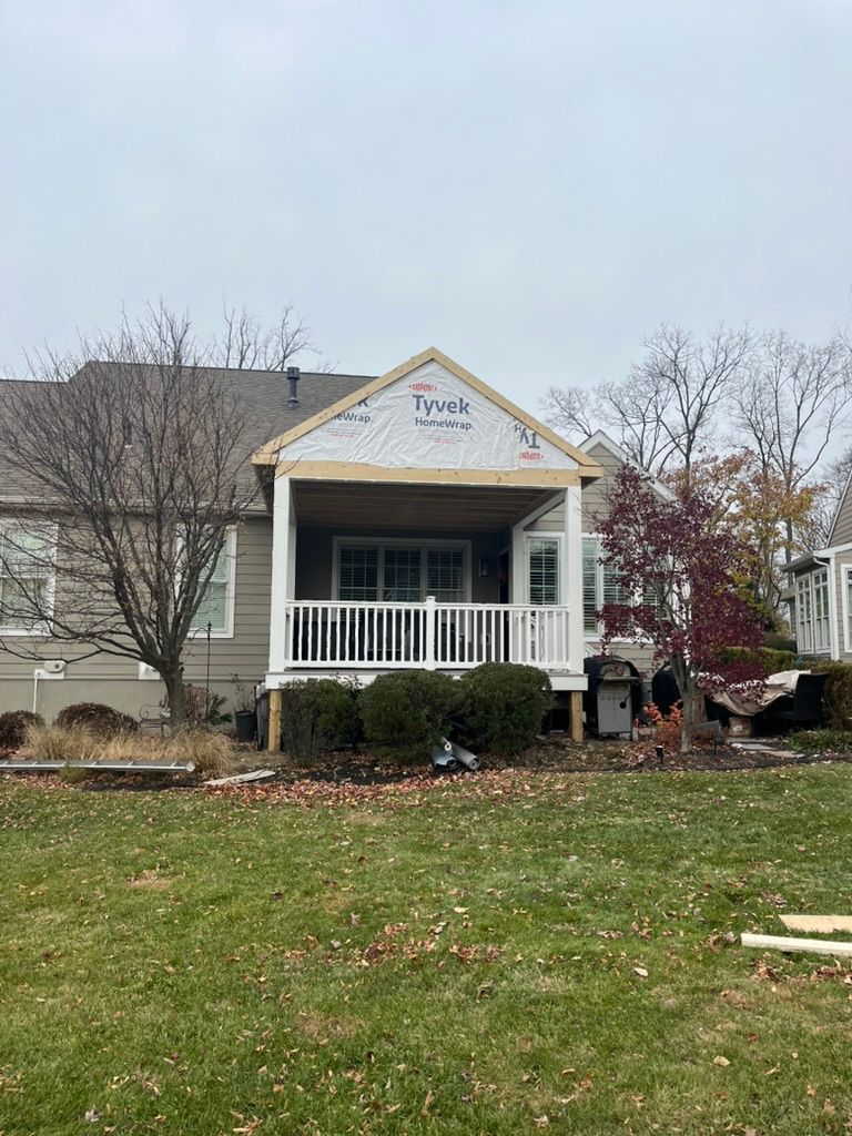 Backyard view of a house with a deck under construction; unfinished roof, white railing, and shrubbery.