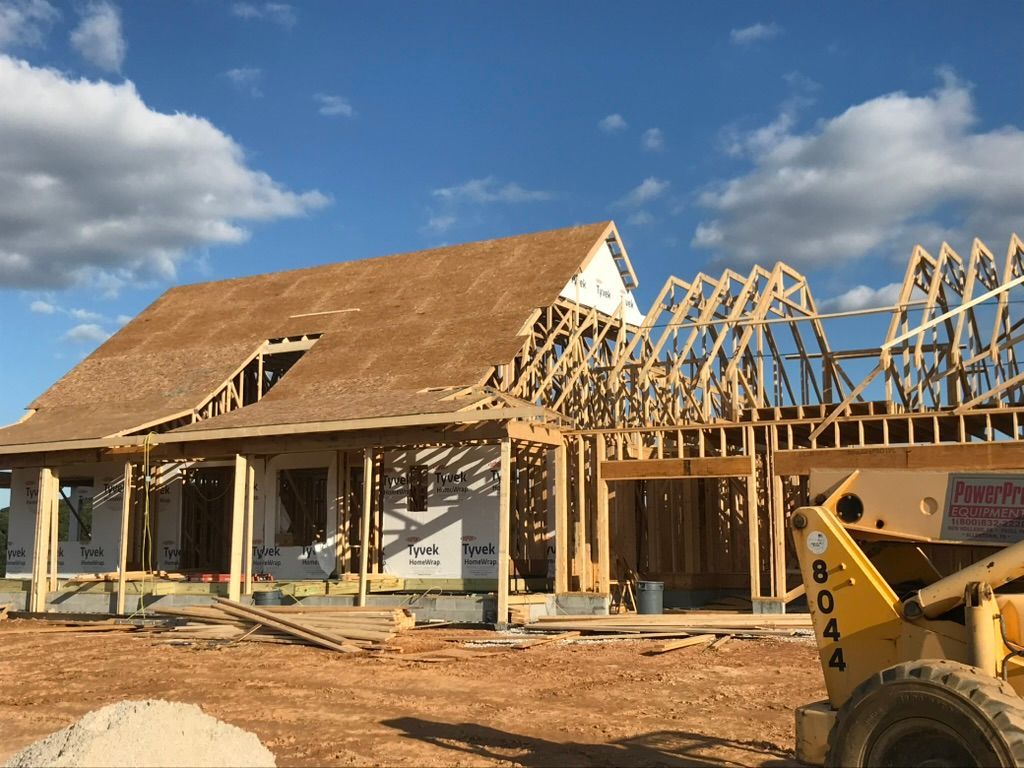 Construction of a house: wooden frame, roof partially covered, blue sky, and a yellow lift.